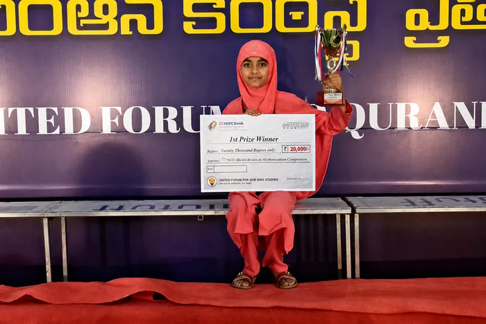 A student on stage with a trophy and a first prize cheque at an inter-school Qur'an competition