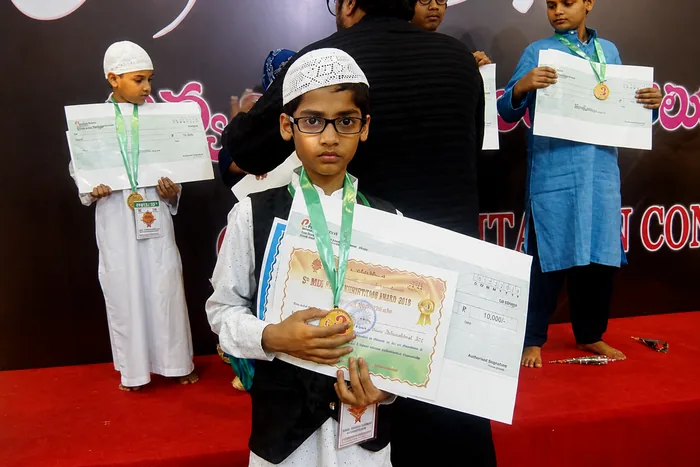 Young students holding certificates and medals won at a recitation competition