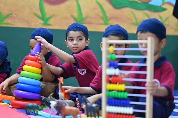 A kindergarten child stacking coloured rings beside the abacus and toy shelf — Peace English Medium School, Kurnool