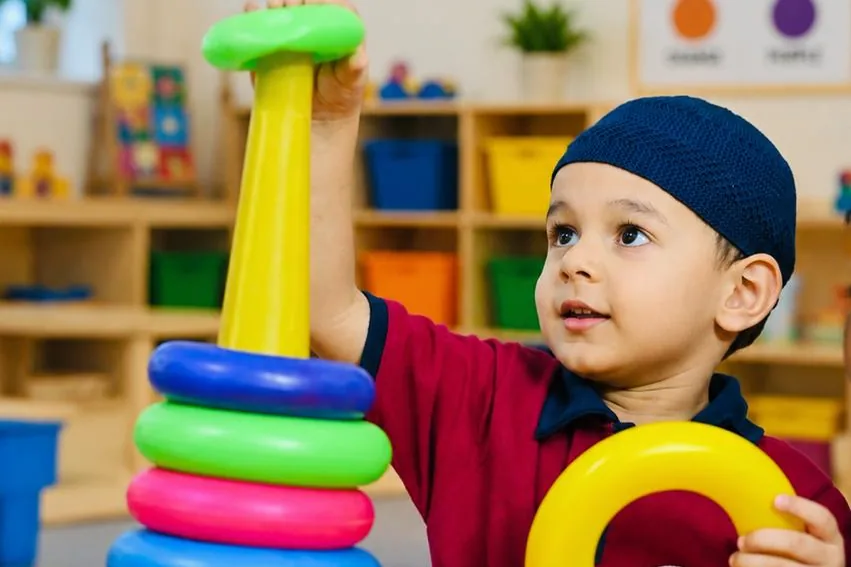 A kindergarten child stacking coloured rings at a table in the activity room